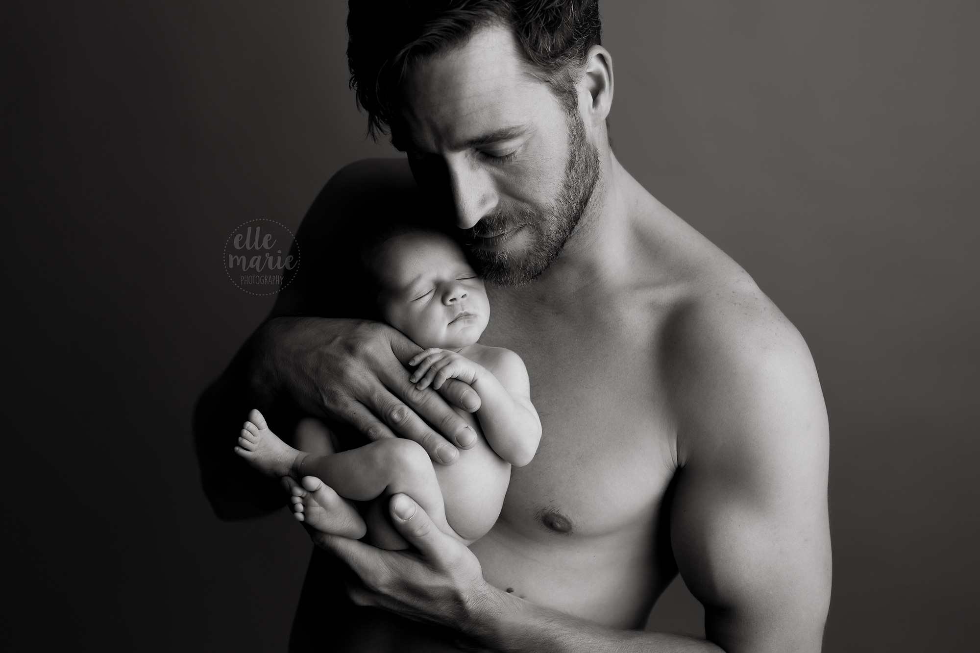 shirtless dad holds newborn baby skin to skin