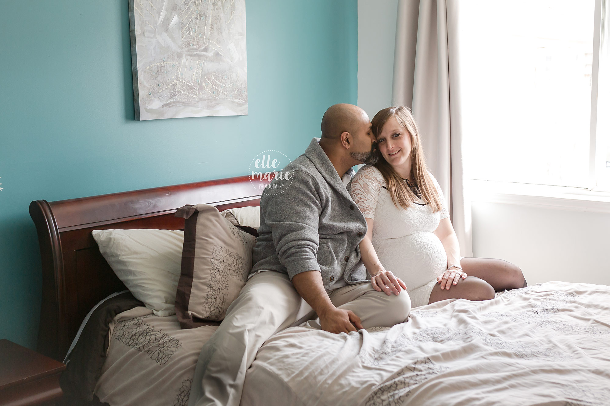 expecting couple on bed in their home steal a kiss