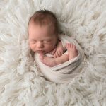 newborn girl wrapped in cream on fur
