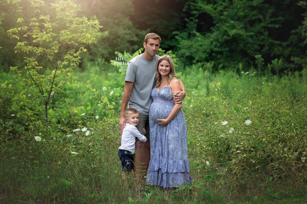 expecting family of 3 pose in a meadow