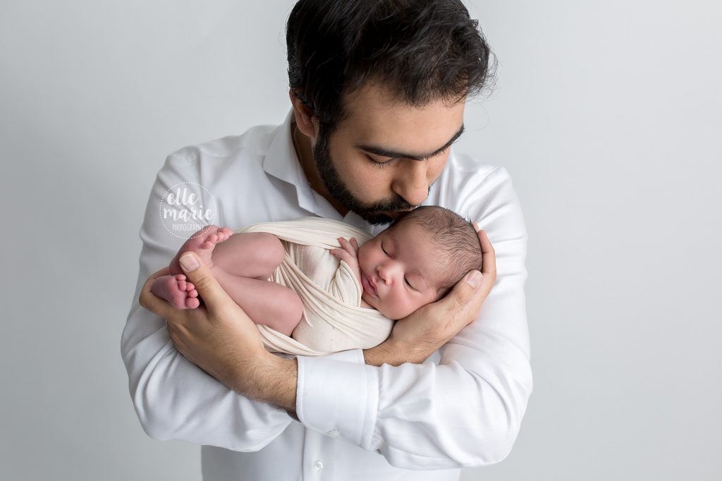 dad holding newborn daughter in arms and kissing her