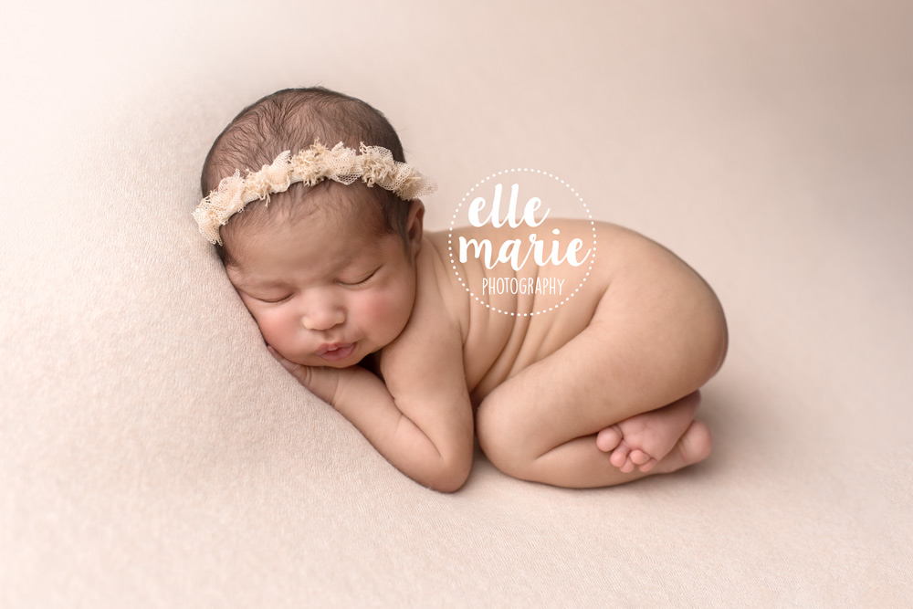 newborn baby girl curled up on pink backdrop