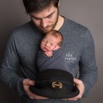 new dad holding newborn baby boy in his pilot hat