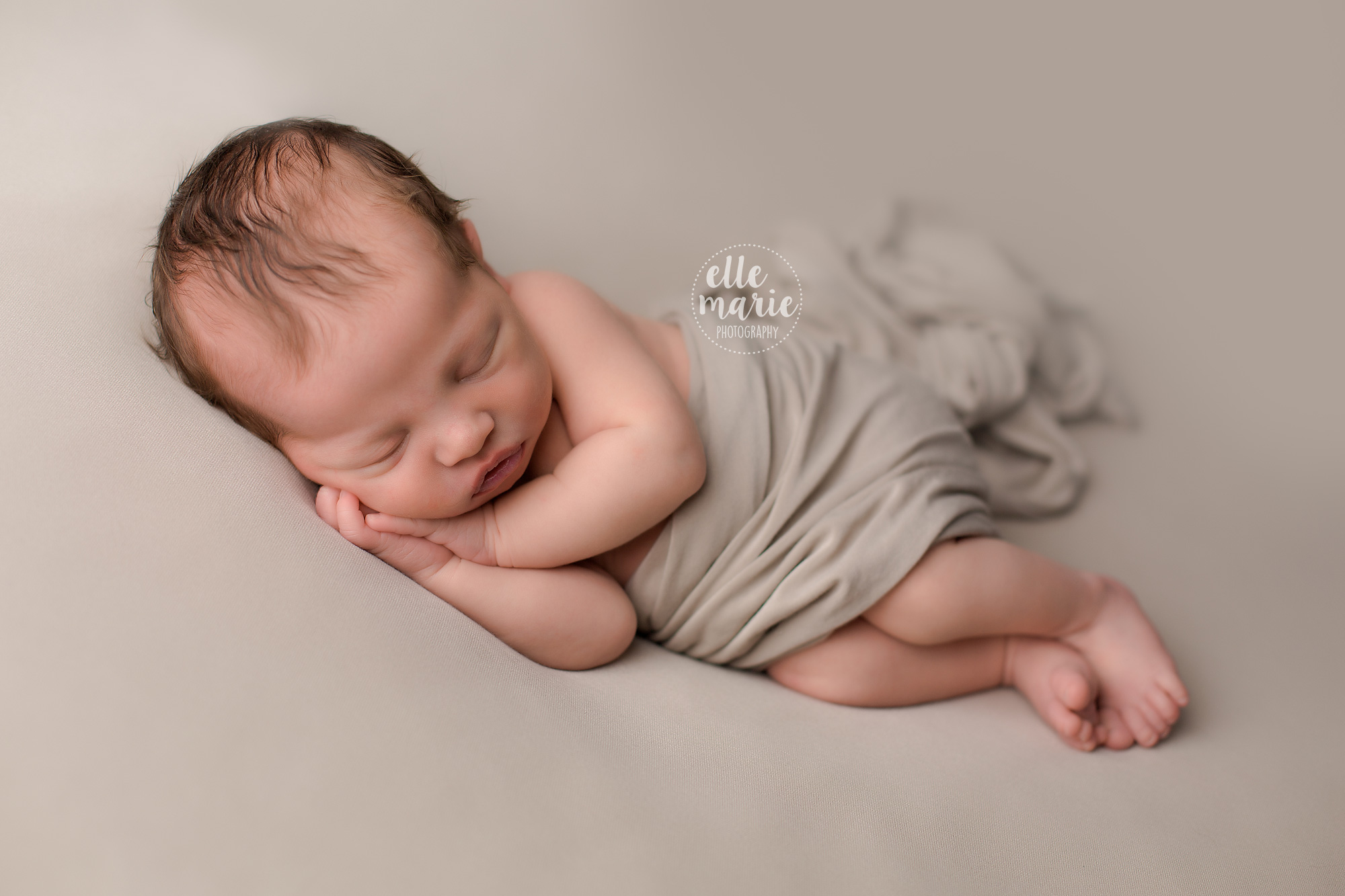 newborn boy laying on his side on a beige backdrop with matching blanket