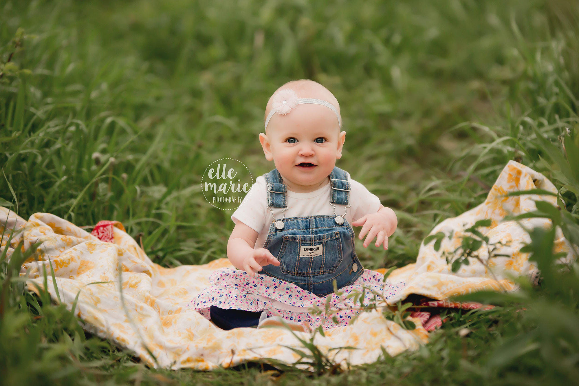 9 month old baby girl sits on quilt in grass