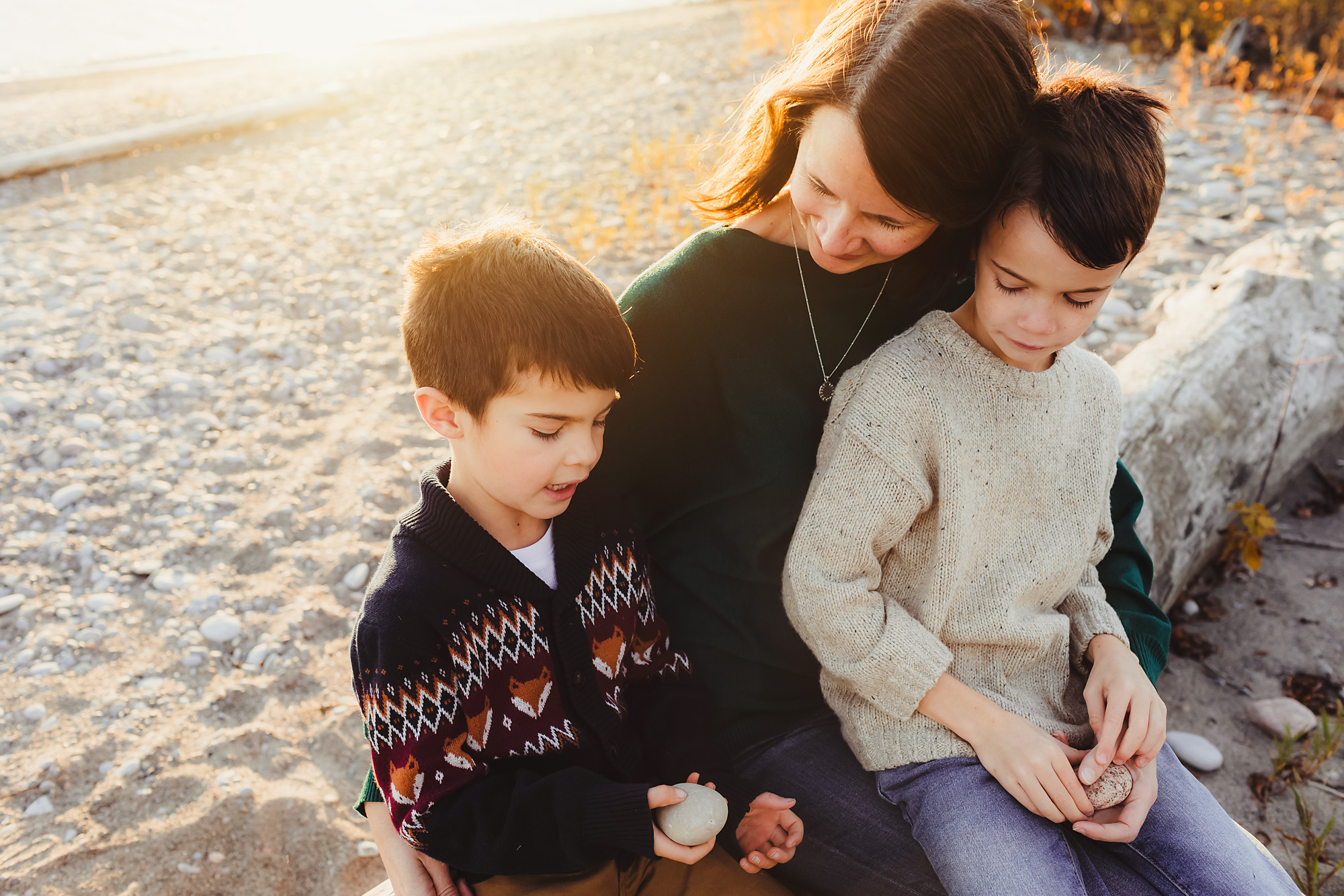 mom sitting with 2 sons on a log by the water at golden hour