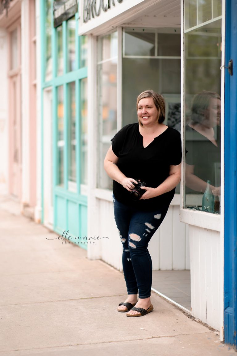 Lyndsey Thomas leaning against a shop in downtown Whitby, holding camera