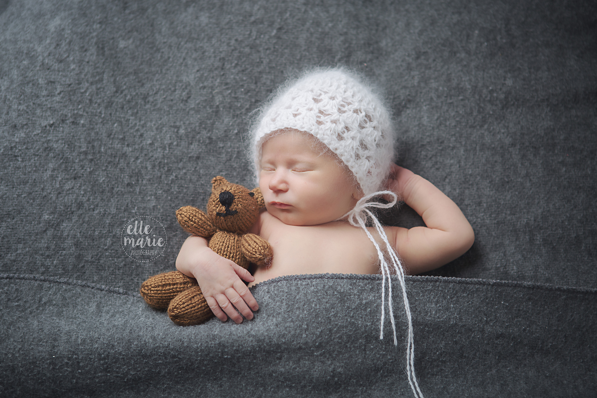newborn baby wearing bonnet with teddy bear