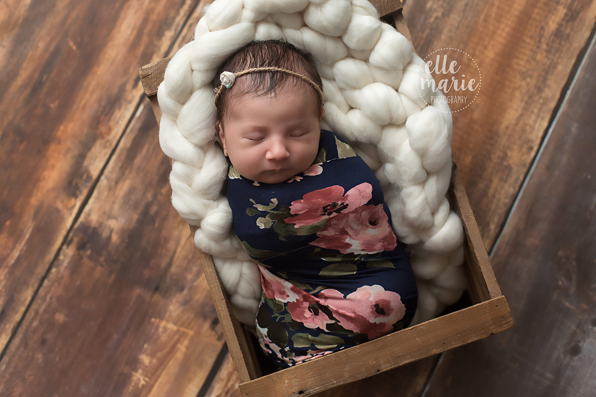 newborn in floral wrap in a brown crate