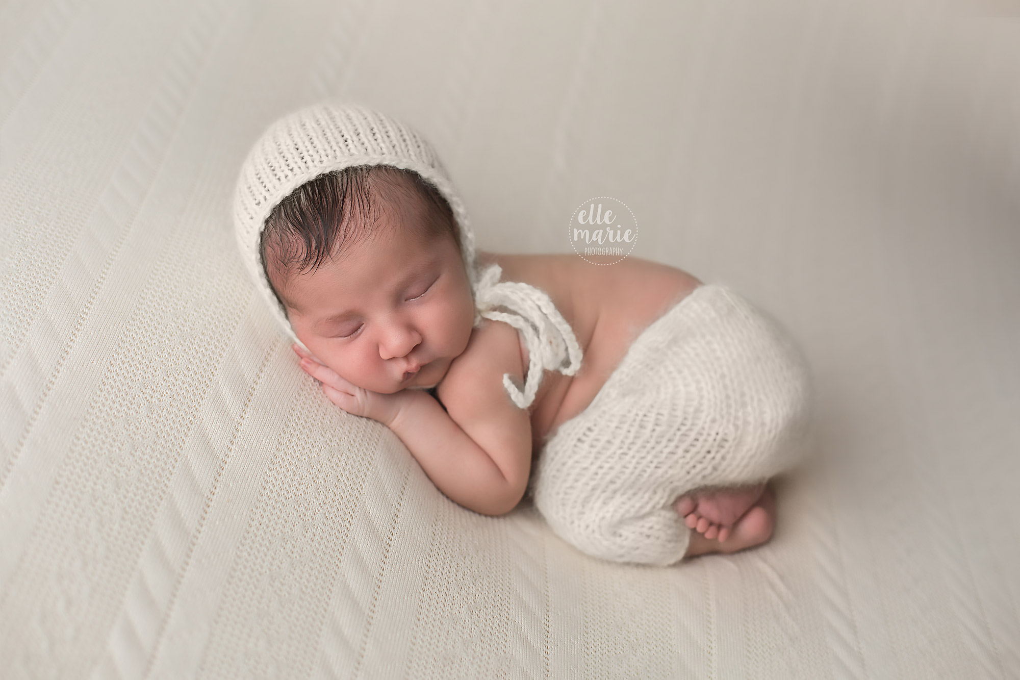 newborn baby dressed in cream with bonnet