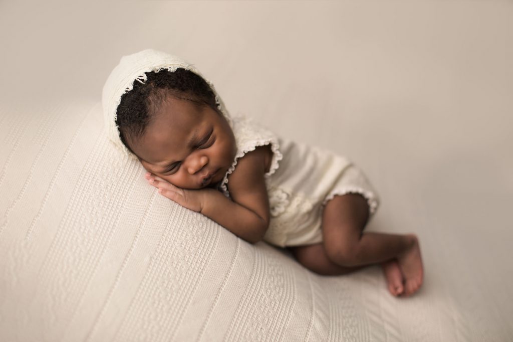 newborn baby girl wearing cream romper and bonnet