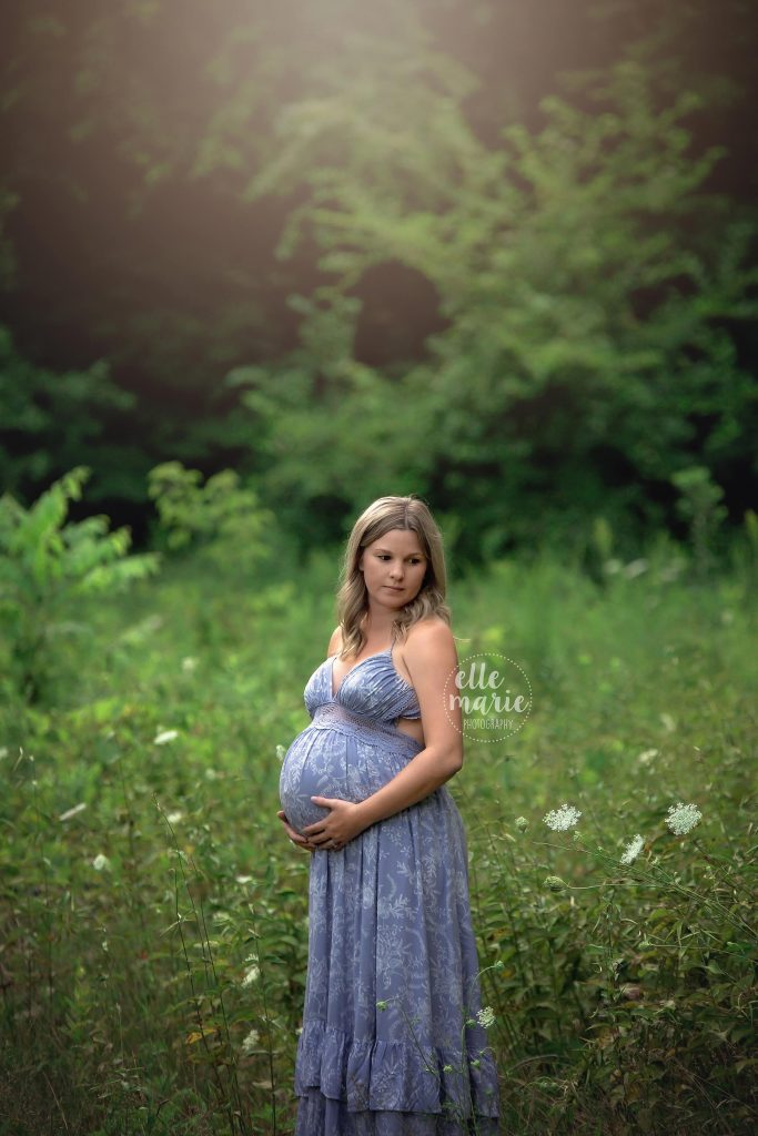 expecting mom holding her belly in a meadow