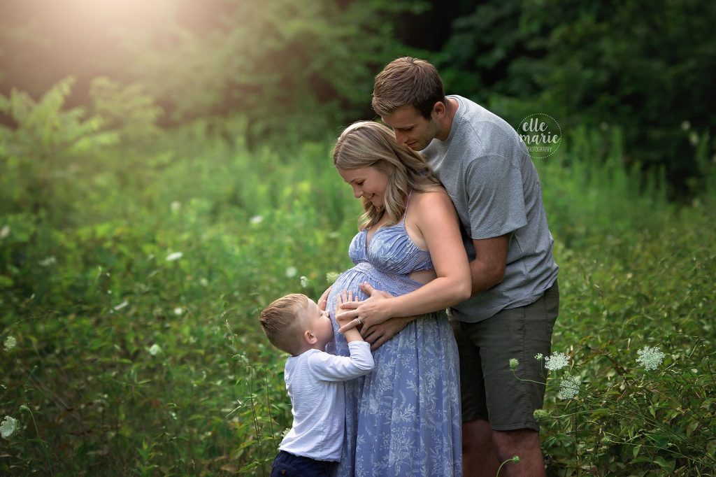 young boy kisses mom's pregnant belly while dad looks on
