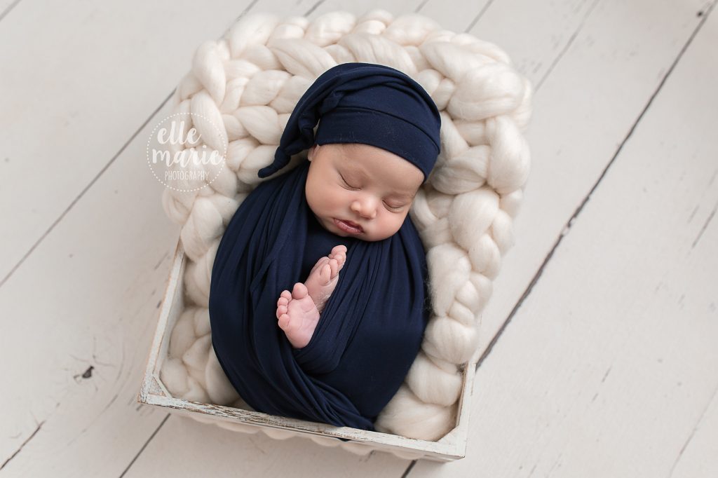 baby boy wrapped in navy in a white crate