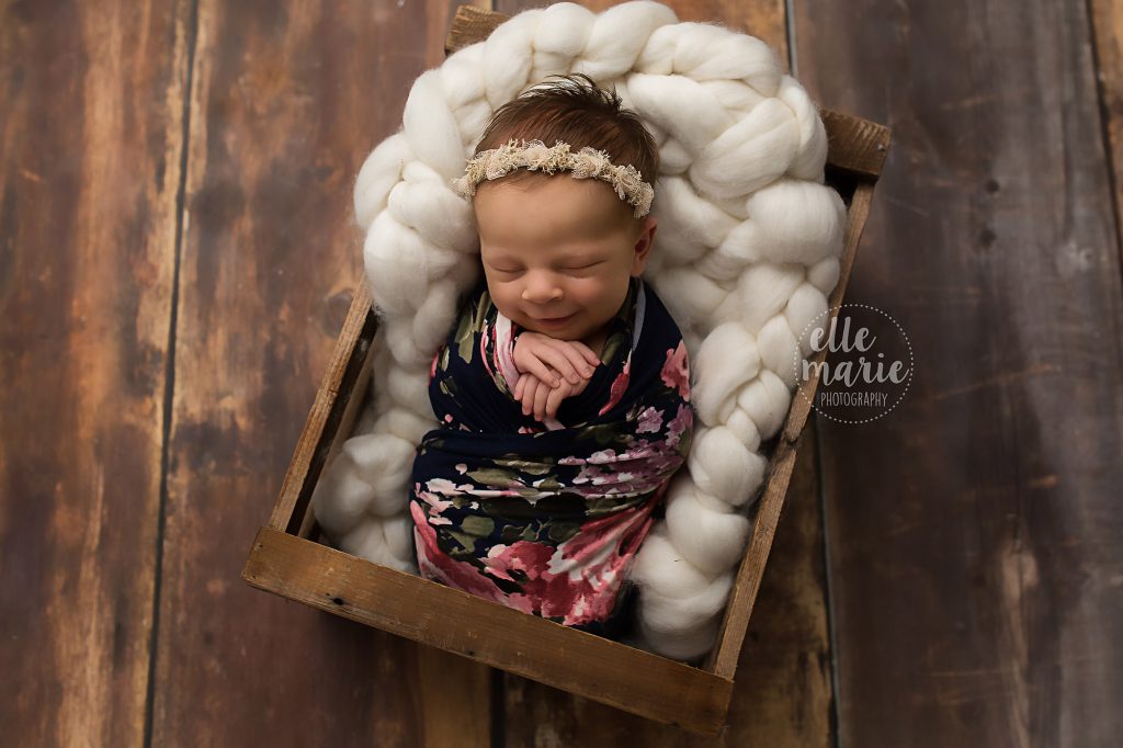 newborn baby girl wrapped in flower fabric in a crate