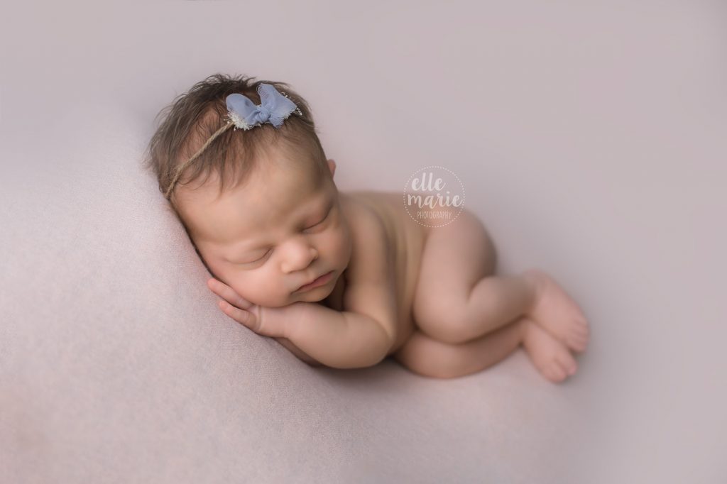 newborn baby girl laying on her side with grey bow on her head