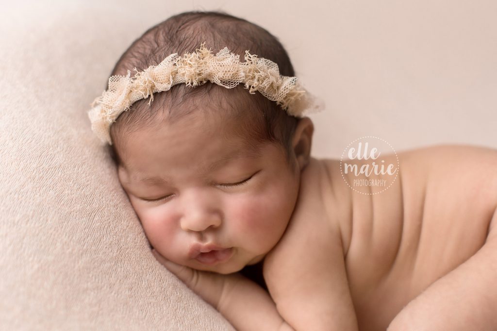 close up of baby girl's face with cream headband on pink backdrop