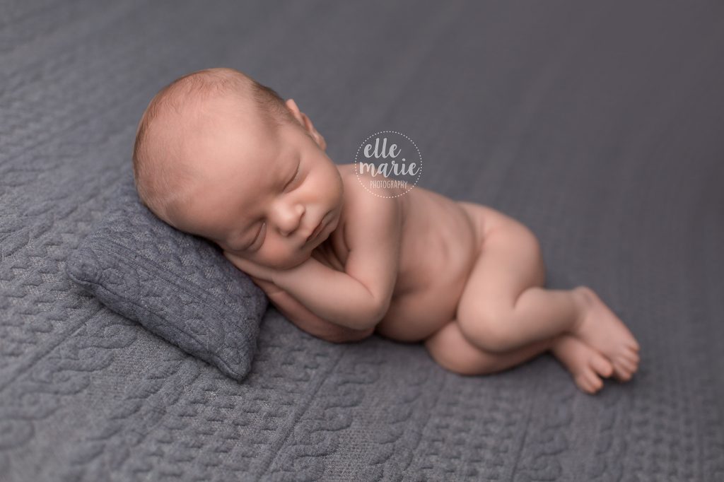 newborn baby boy sidelaying on grey pillow and backdrop