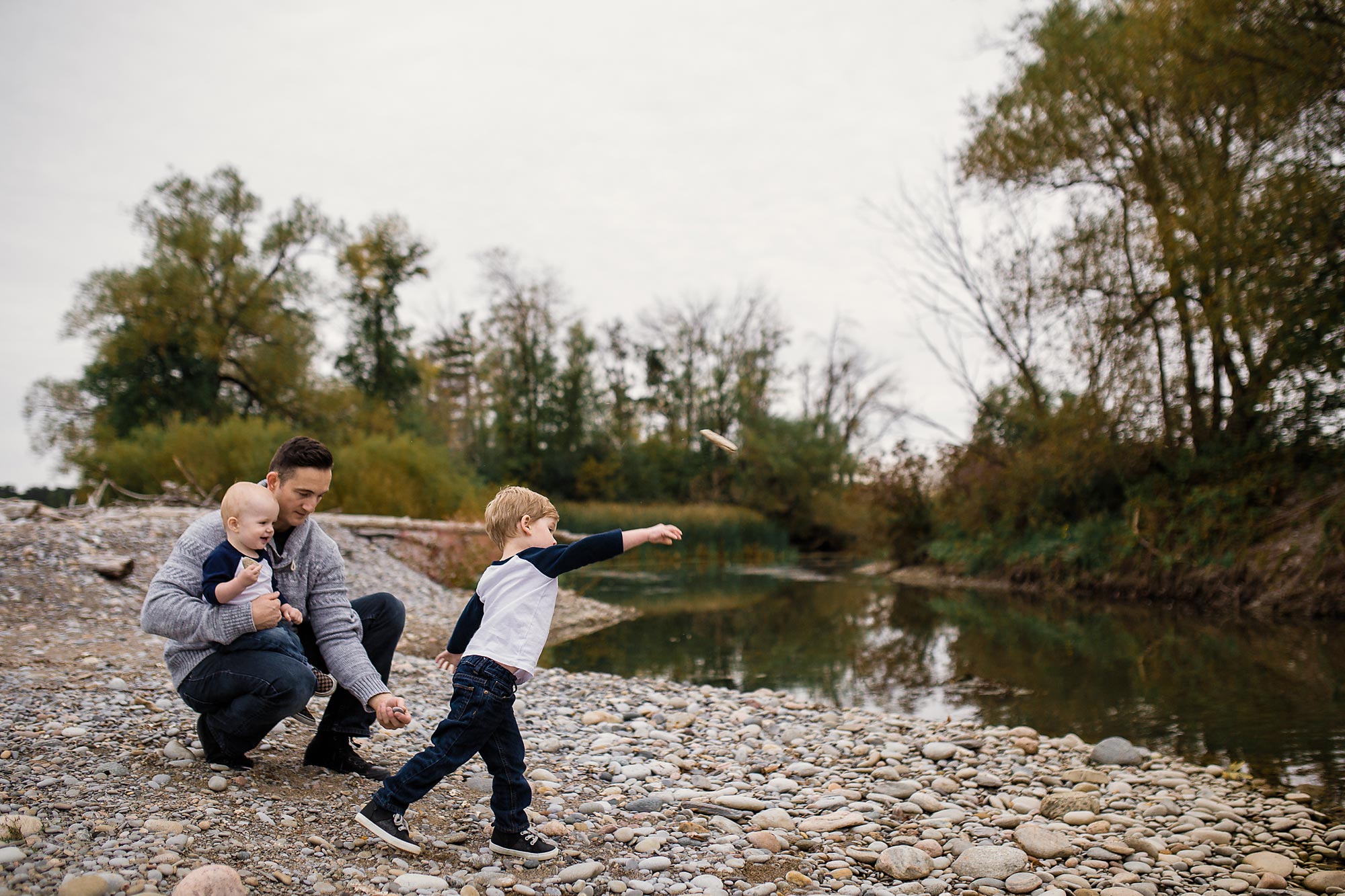 brothers throwing rocks in pond with dad