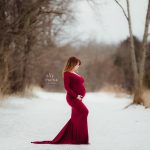 expecting mother in red gown in winter setting looking at belly