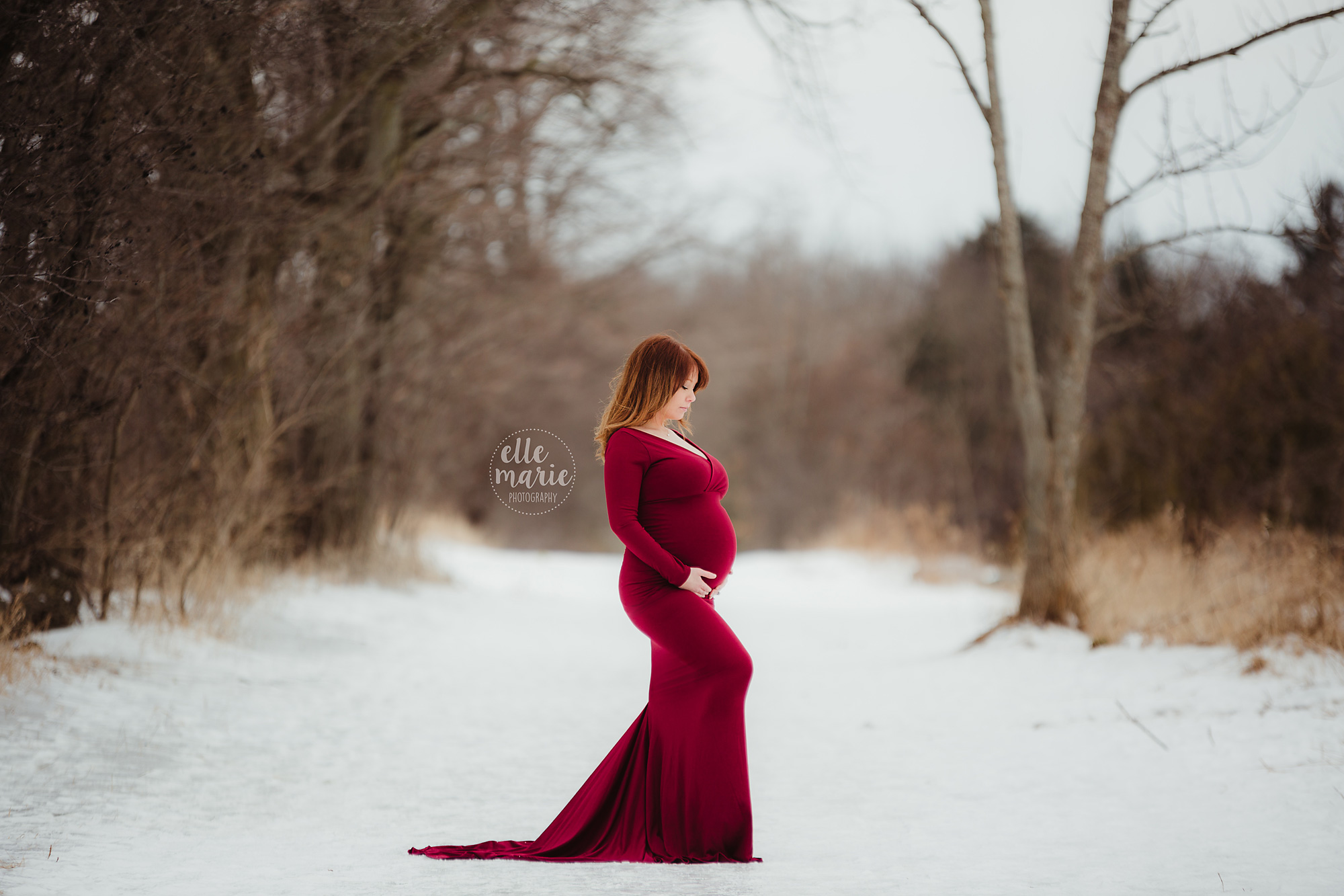 expecting mother in red gown in winter setting looking at belly