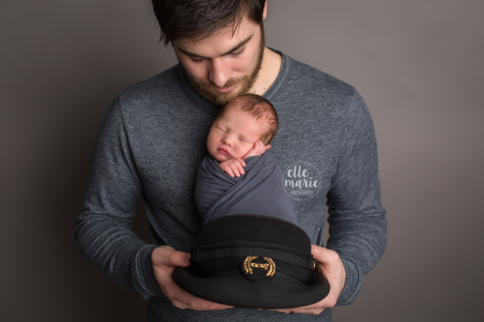 new dad holding newborn baby boy in his pilot hat