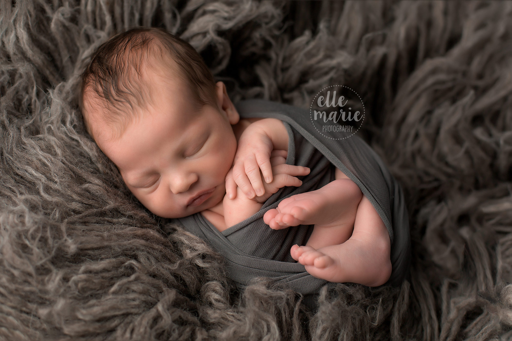newborn boy wrapped in grey on a grey rug