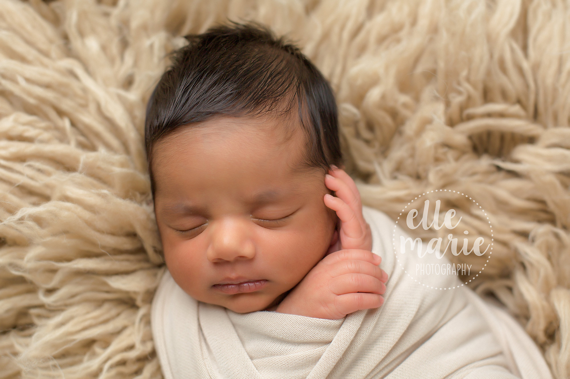 baby boy on tan rug wrapped in tan swaddle