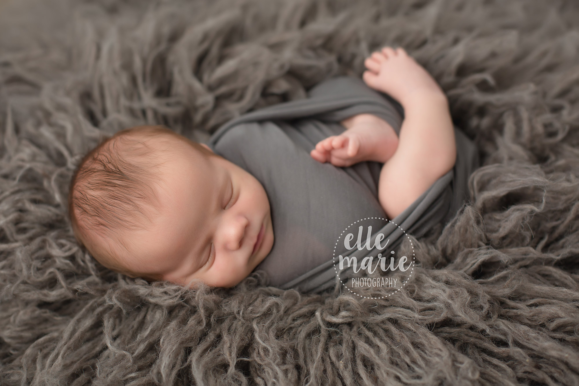 Newborn baby boy on grey fur rug