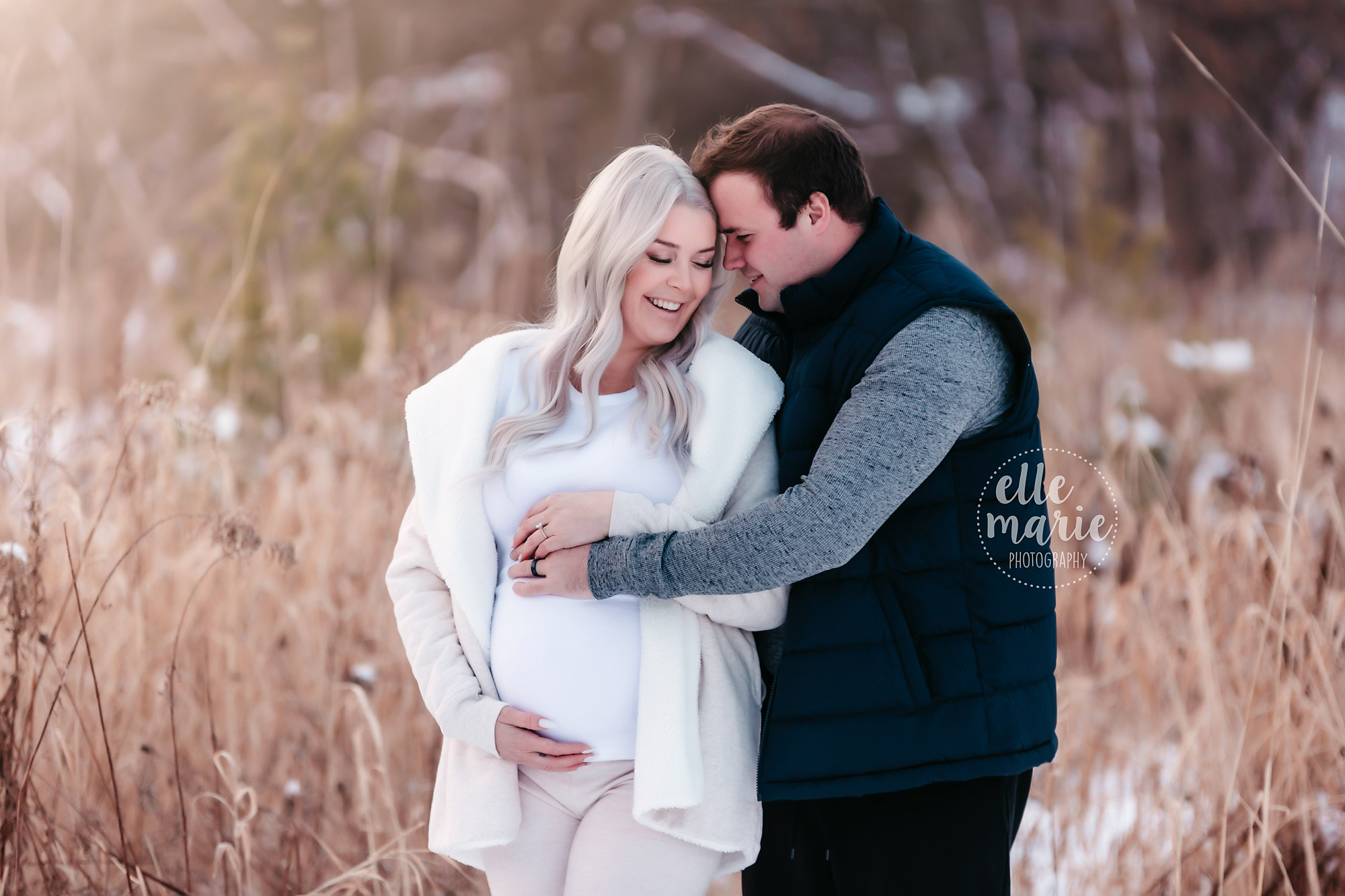 expecting couple shares a laugh while embracing outside in the snow