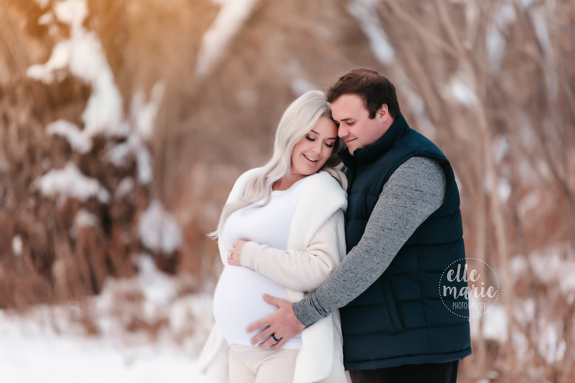 expecting couple snuggle in the snow