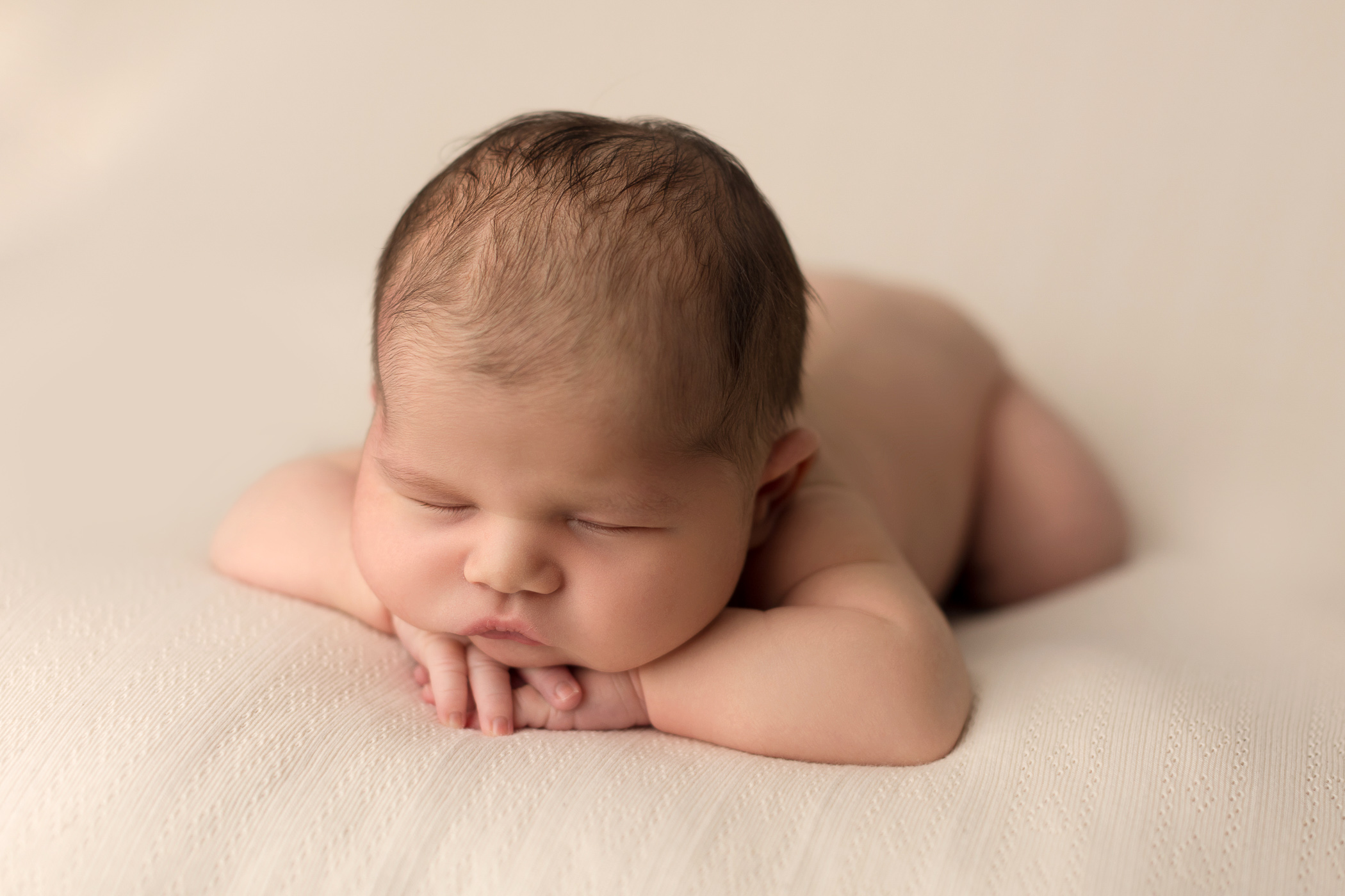 mewborn baby laying with head on hands