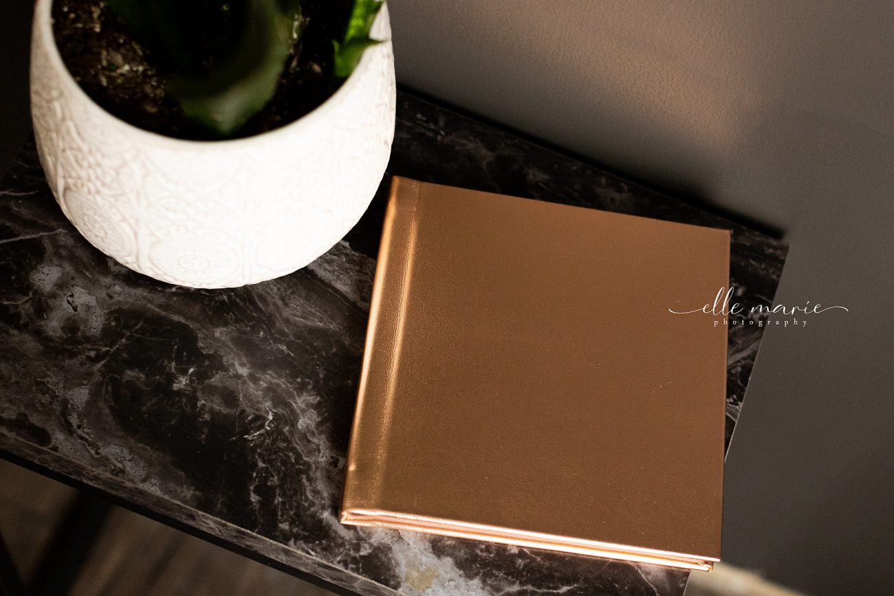 gold cover boudoir album sitting closed on a table with a plant beside it.