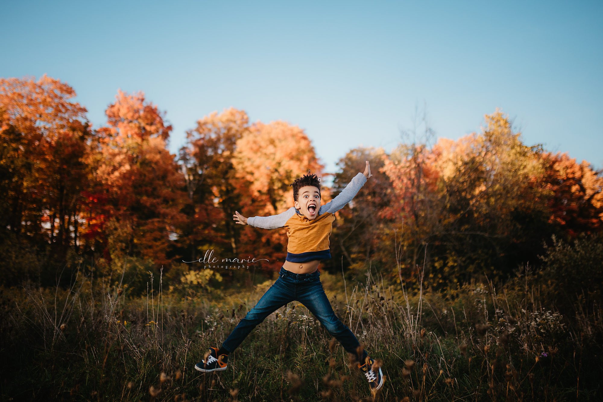 young boy jumping for joy in fall coloured leaves