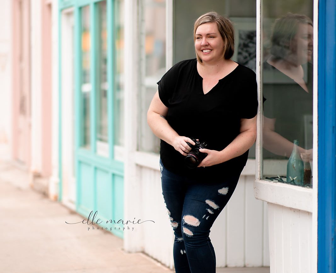 Lyndsey Thomas leaning against a shop in downtown Whitby, holding camera
