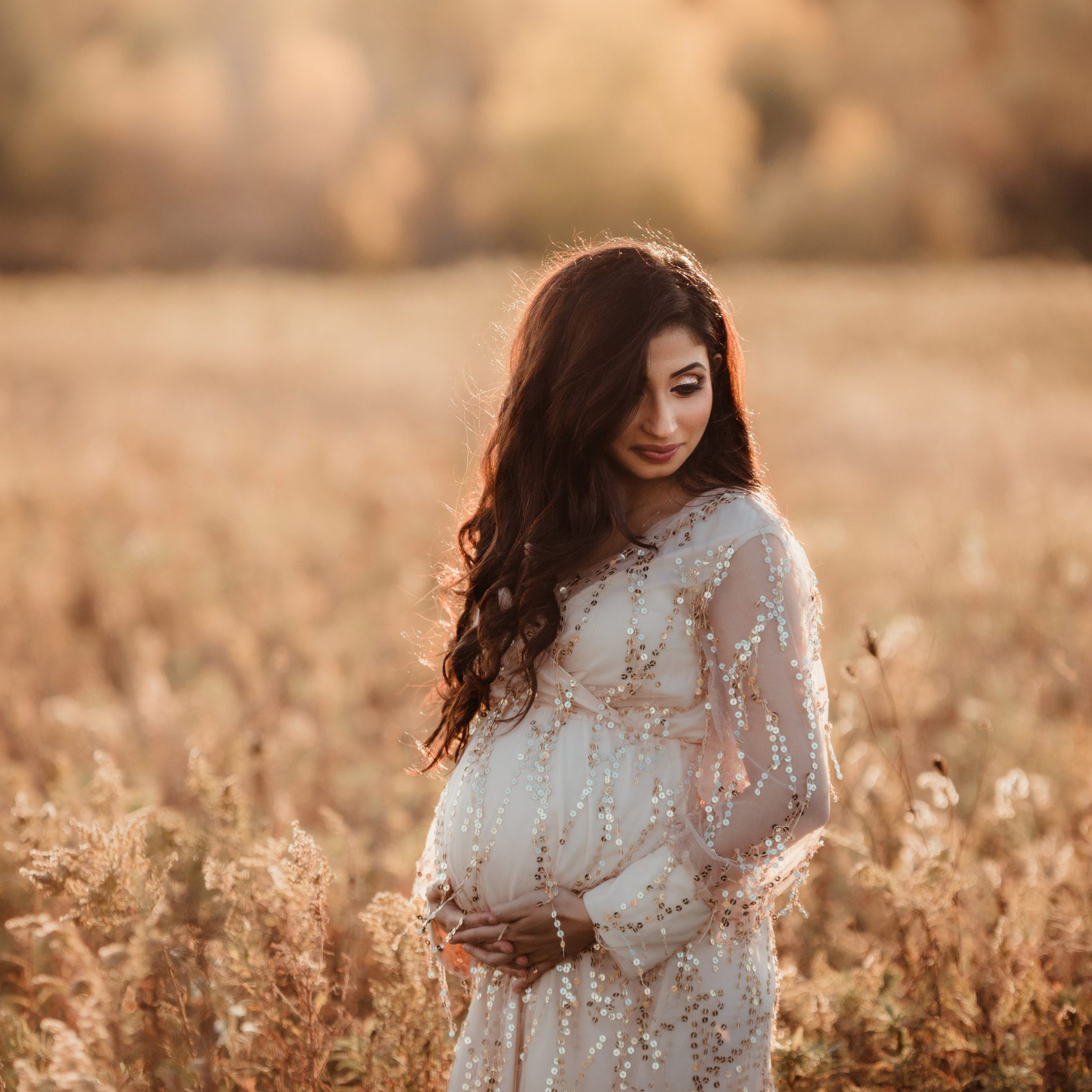 pregnant mom standing in a field at sunset