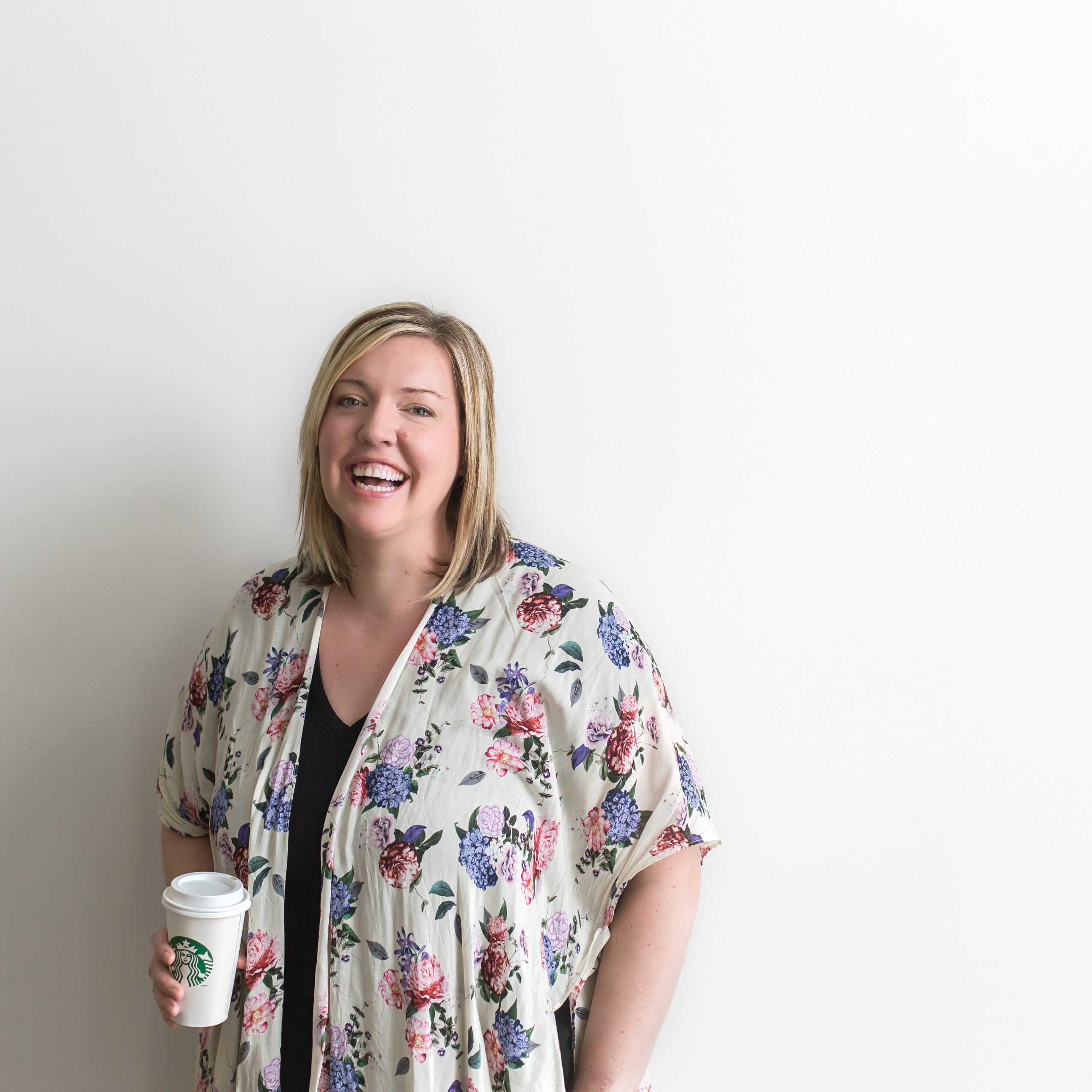 Lyndsey Thomas Standing against a white wall holding a starbucks cup
