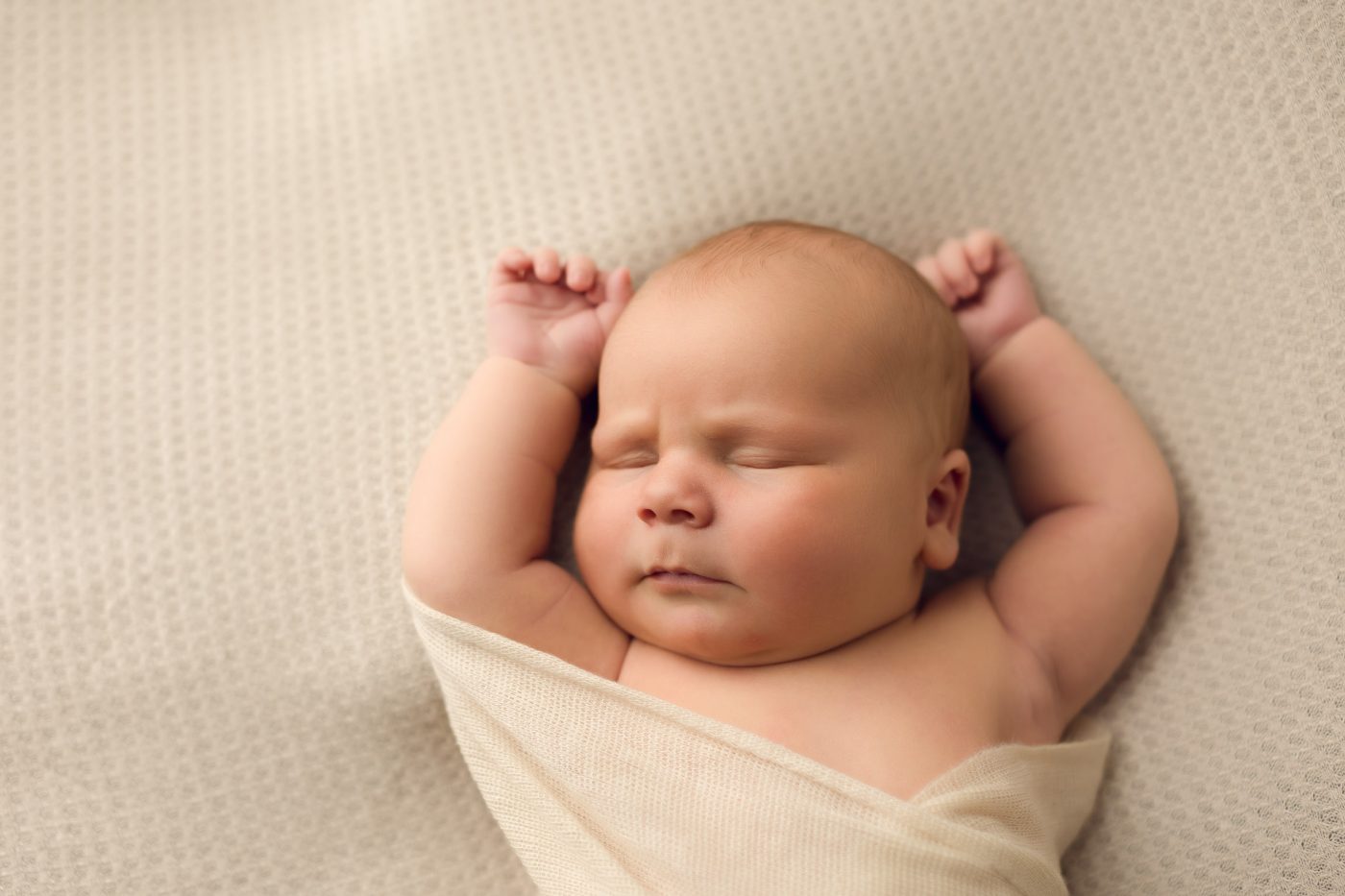 newborn baby lays with arms overhead