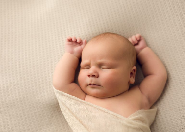 newborn baby lays with arms overhead