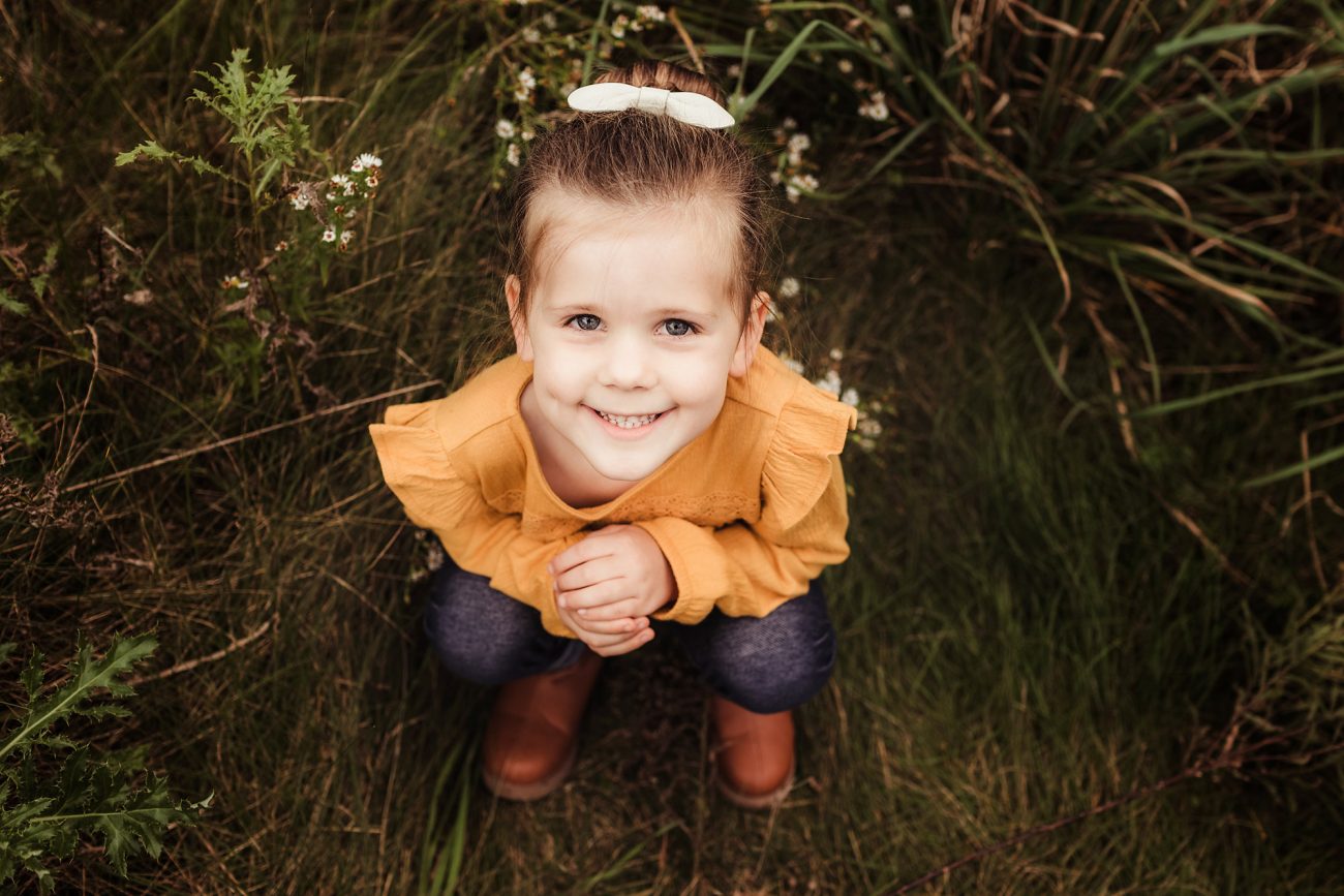 young girl sitting in a field smiling at camera