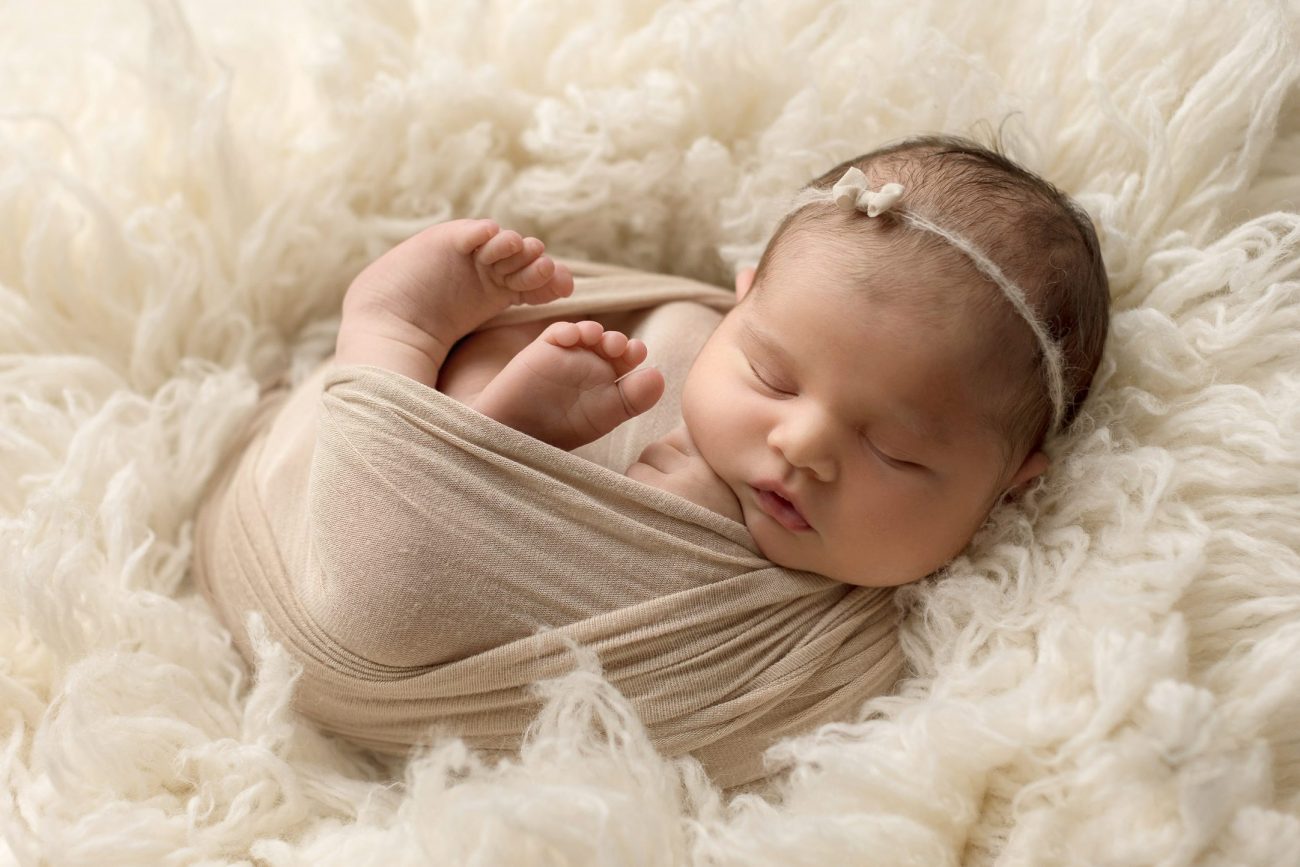 baby wrapped in cream, on a fluffy rug, wearing a simple headband
