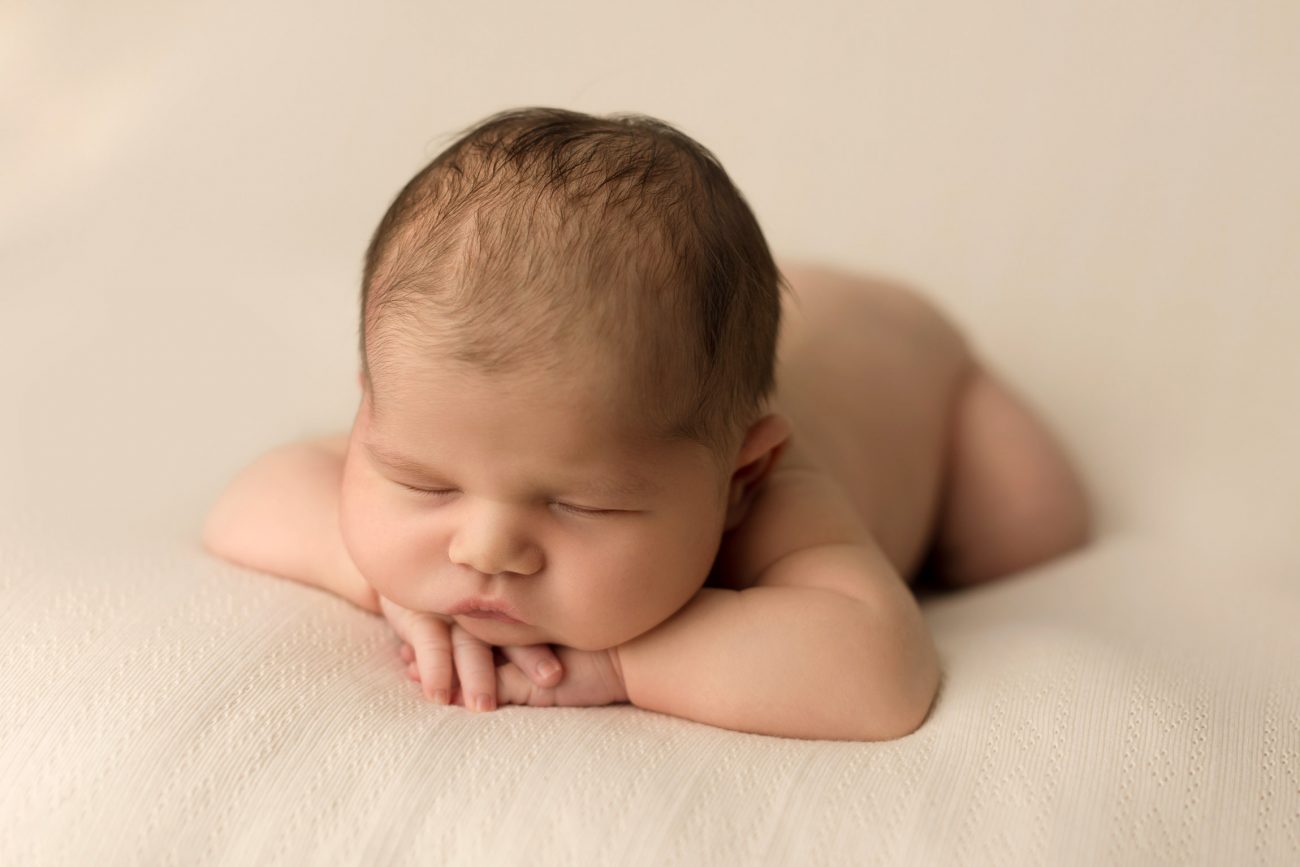 baby laying on cream blanket, resting head on hands