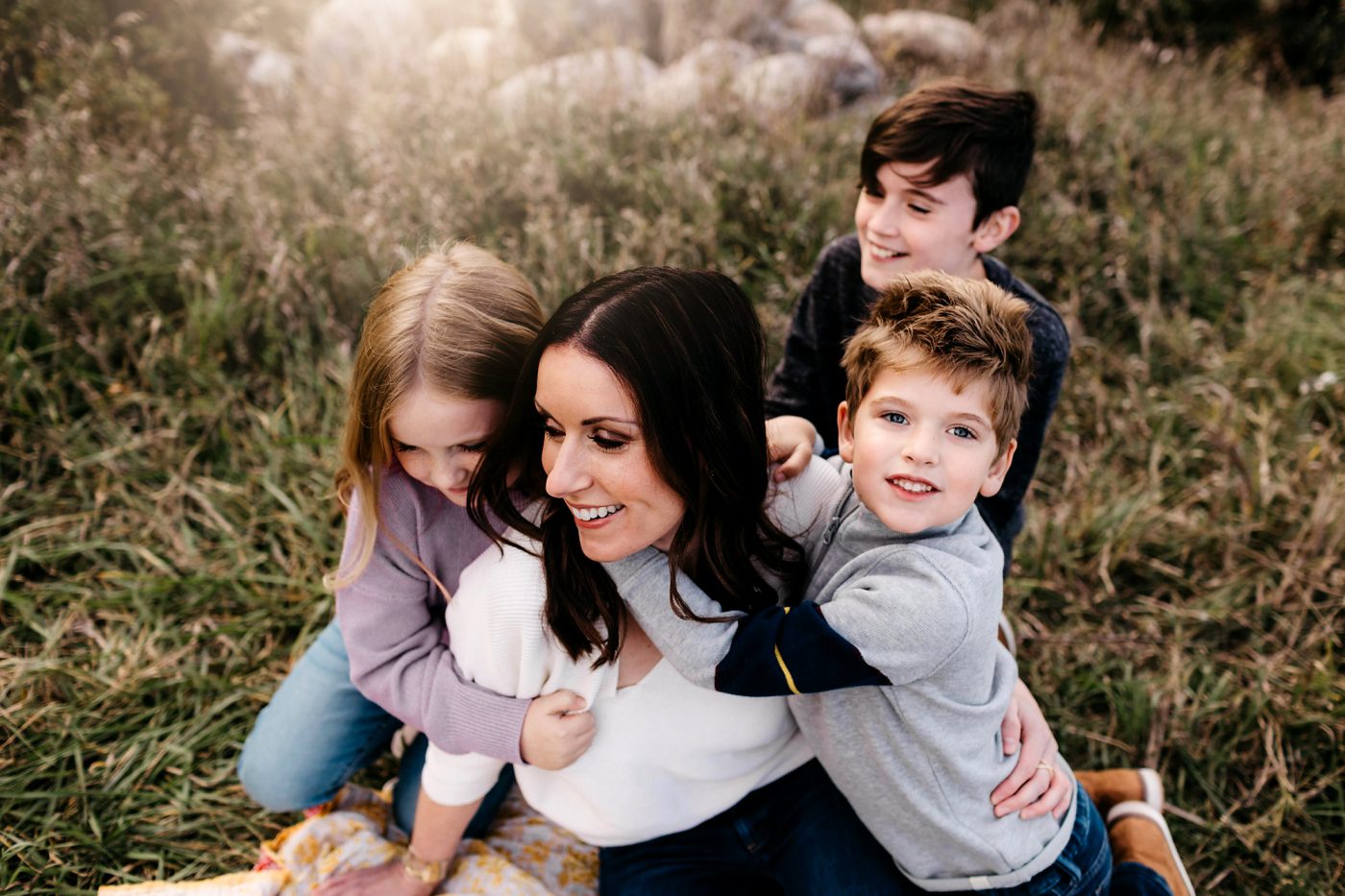 mom sitting in grass being hugged by her 3 children