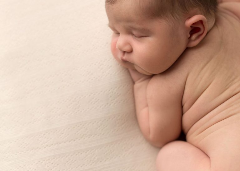 A newborn baby sleeps in froggy pose on a white bed in a studio after a 3d ultrasound whitby