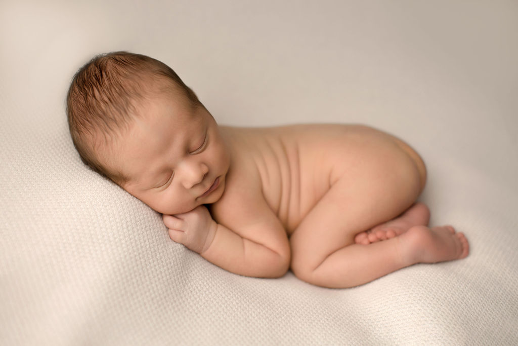 A newborn baby sleeps in froggy pose on a bean bag in a studio