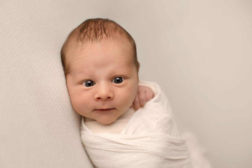 A newborn baby lays on a white bed in a swaddle with eyes wide open after visiting baby shack whitby