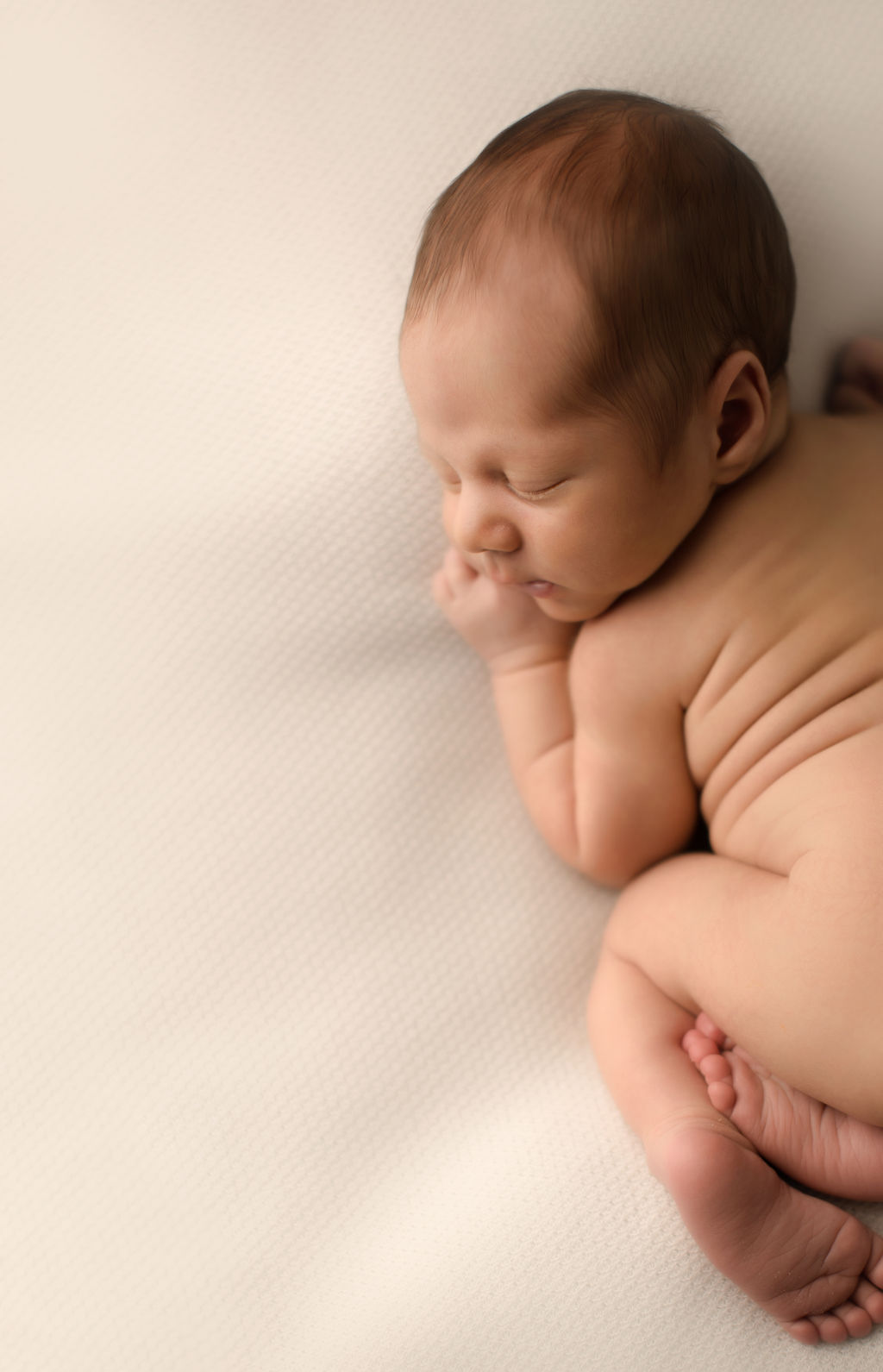 A newborn baby sleeps in froggy pose naked on a white bed after visiting baby shack whitby