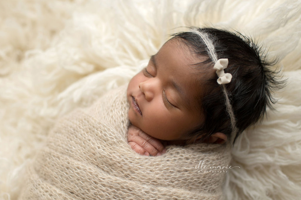 A newborn baby sleeps in a knit blanket on a white fur blanket after visiting baby store oshawa