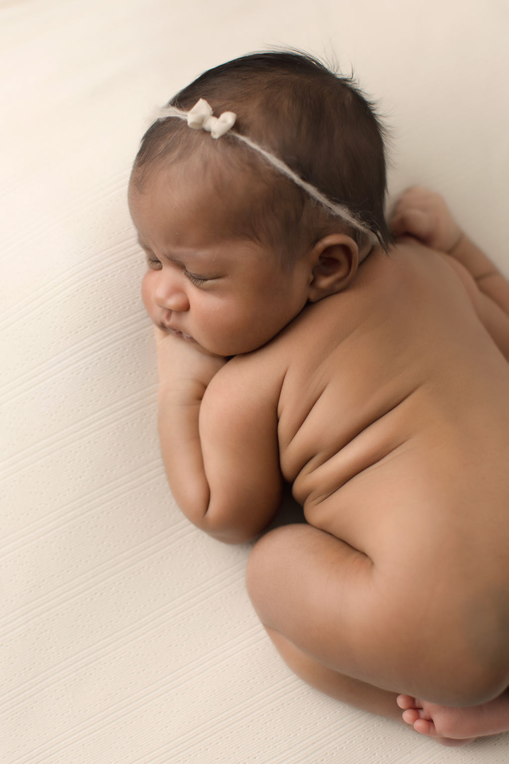 A newborn baby sleeps in froggy pose on a white pad naked