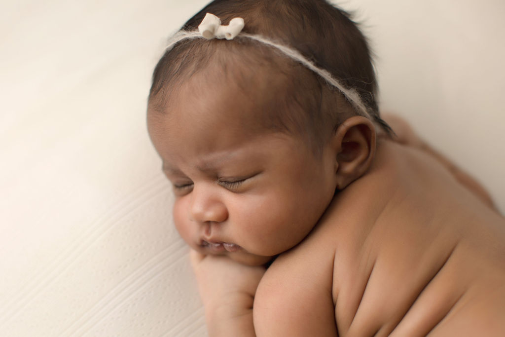 Details of a sleeping newborn baby on a white pad in a studio with a small white bow headband thanks to cloth diaper service Oshawa
